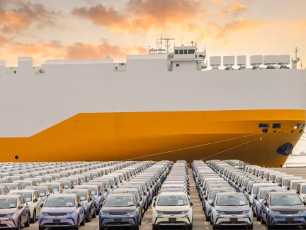 new cars parked in front of a ship in the harbour