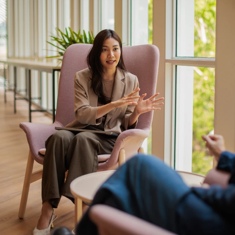Asian Lady sitting in a chair talking to a colleague, sharing knowledge