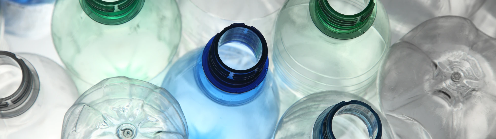Overhead close-up: Empty, clear plastic bottles (caps removed, some green/blue tint) emphasizing plastic recycling.