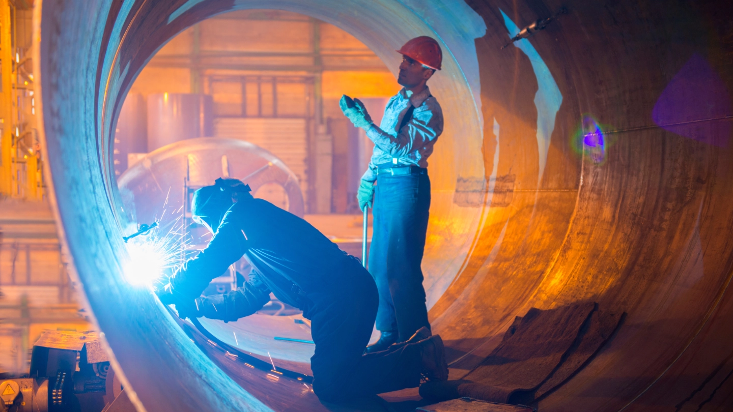 Two male welders working on metal pipe image