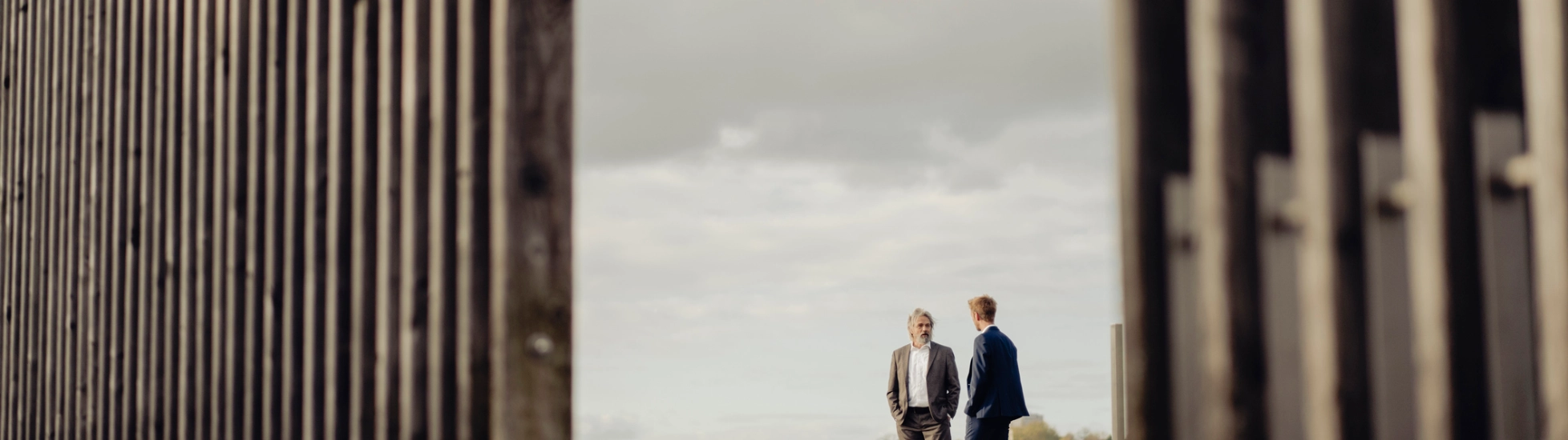 Two businessmen standing behind fencing