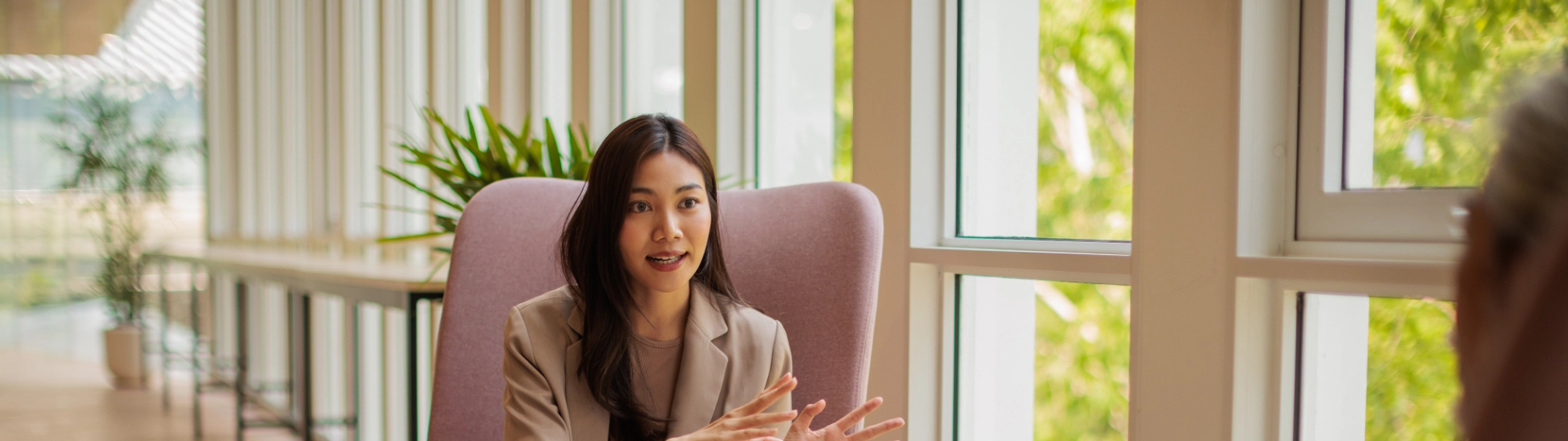 Asian Lady sitting in a chair talking to a colleague, sharing knowledge