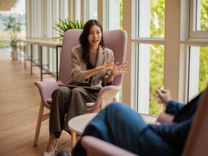 Asian Lady sitting in a chair talking to a colleague, sharing knowledge